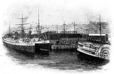 Docking pier with wooden buildings, Seattle skyline behind; 'Olympus', a paddlewheel ferry.