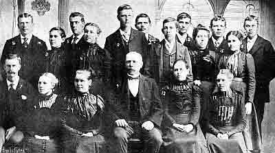 Rev. Foss with a group of mostly young adults; some sitting, some standing, all in Sunday best.